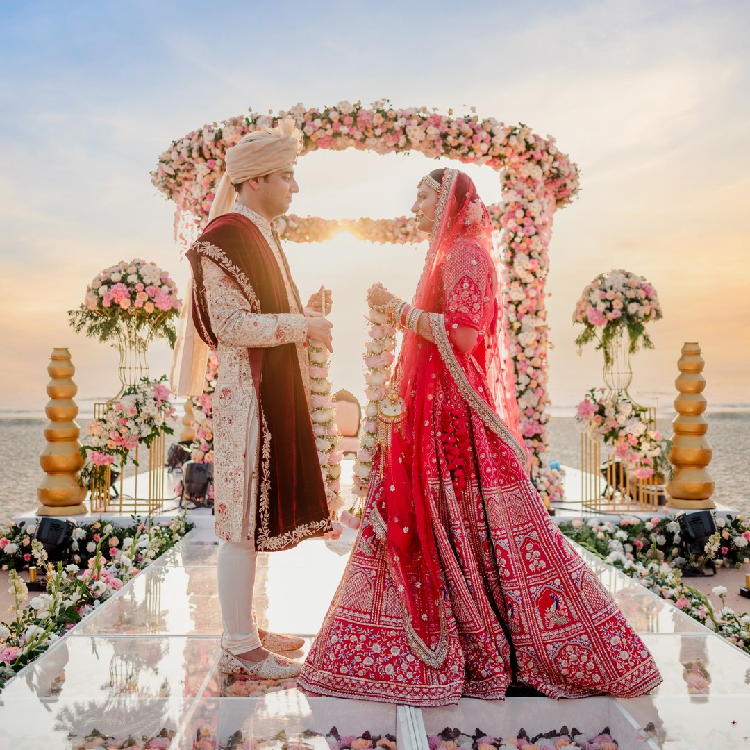 Bride and groom under a floral mandap on a beach at sunset